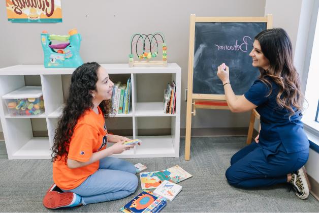 A student writing on small chalkboard and another student watching